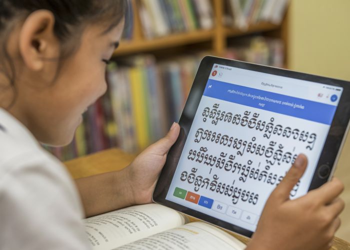 Student happily learning Central Khmer language with textbook and app.