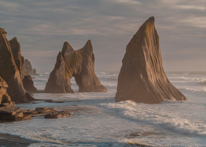 Rocky coastline with sea stacks and arches formed by wave erosion. Waves crash against the shore, highlighting the power of the ocean.