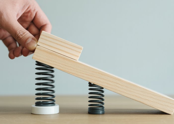 Hand pushing wooden block up an inclined plane with spring scale showing force measurement.