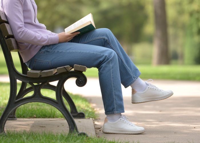 Person reading a book comfortably on a park bench of standard height.