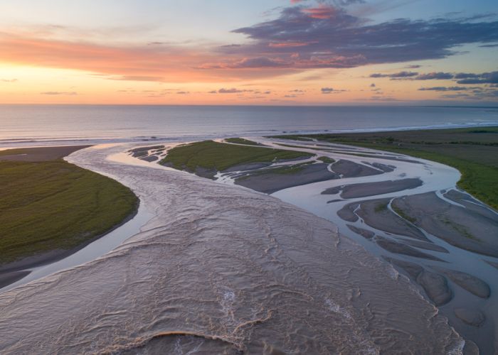 River discharge flowing into the ocean during a vibrant sunset, illustrating the concept of the volume of water a river carries.