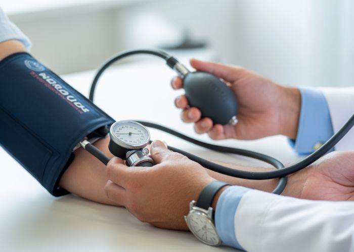 Doctor measuring blood pressure using a stethoscope and sphygmomanometer, listening for Korotkoff sounds.