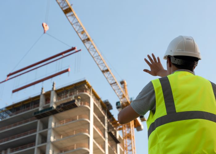 Construction worker signaling to a tower crane operator lifting a steel beam on a skyscraper construction site.